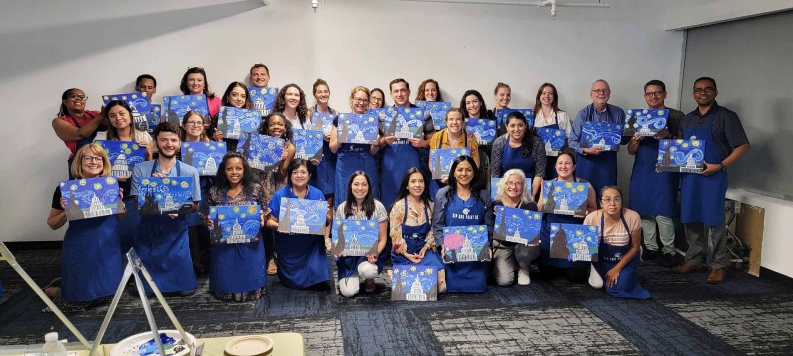 A paint and sip gathering captures a group of people posing with their paintings