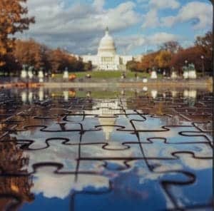 The United States Capitol building is reflected on a wet surface with what appears to be a jigsaw puzzle overlay, creating an artistic blend of reality and graphic alteration, reminiscent of a paint and sip session in