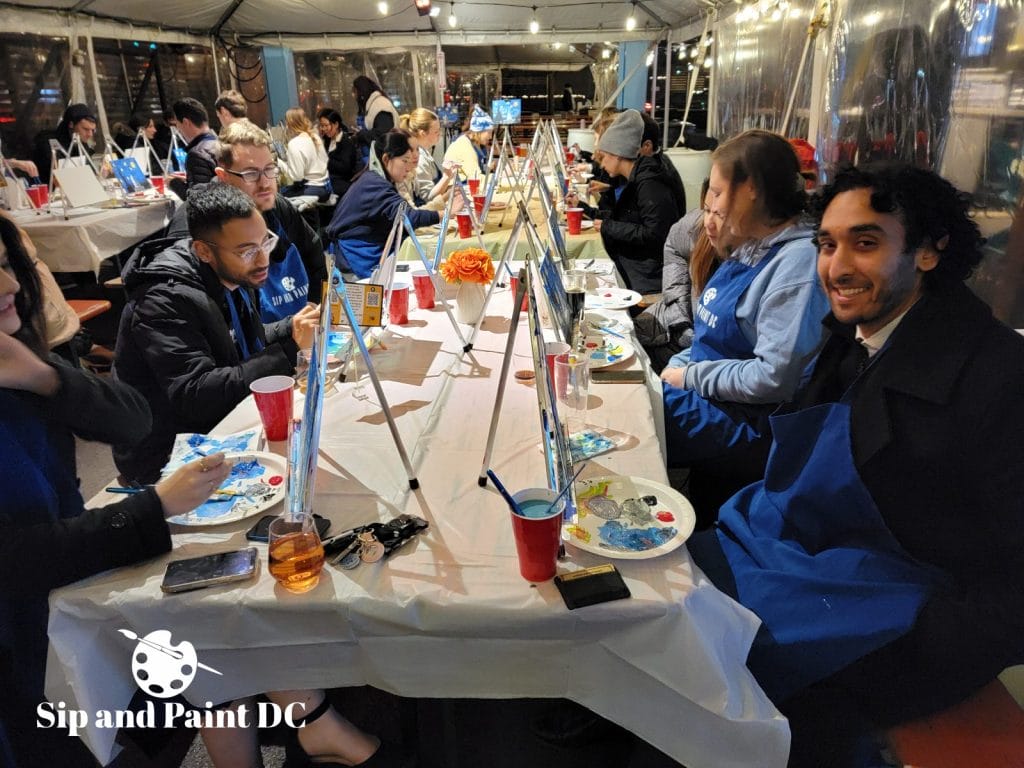 People participating in a group painting session at an outdoor event called "sip and paint dc.