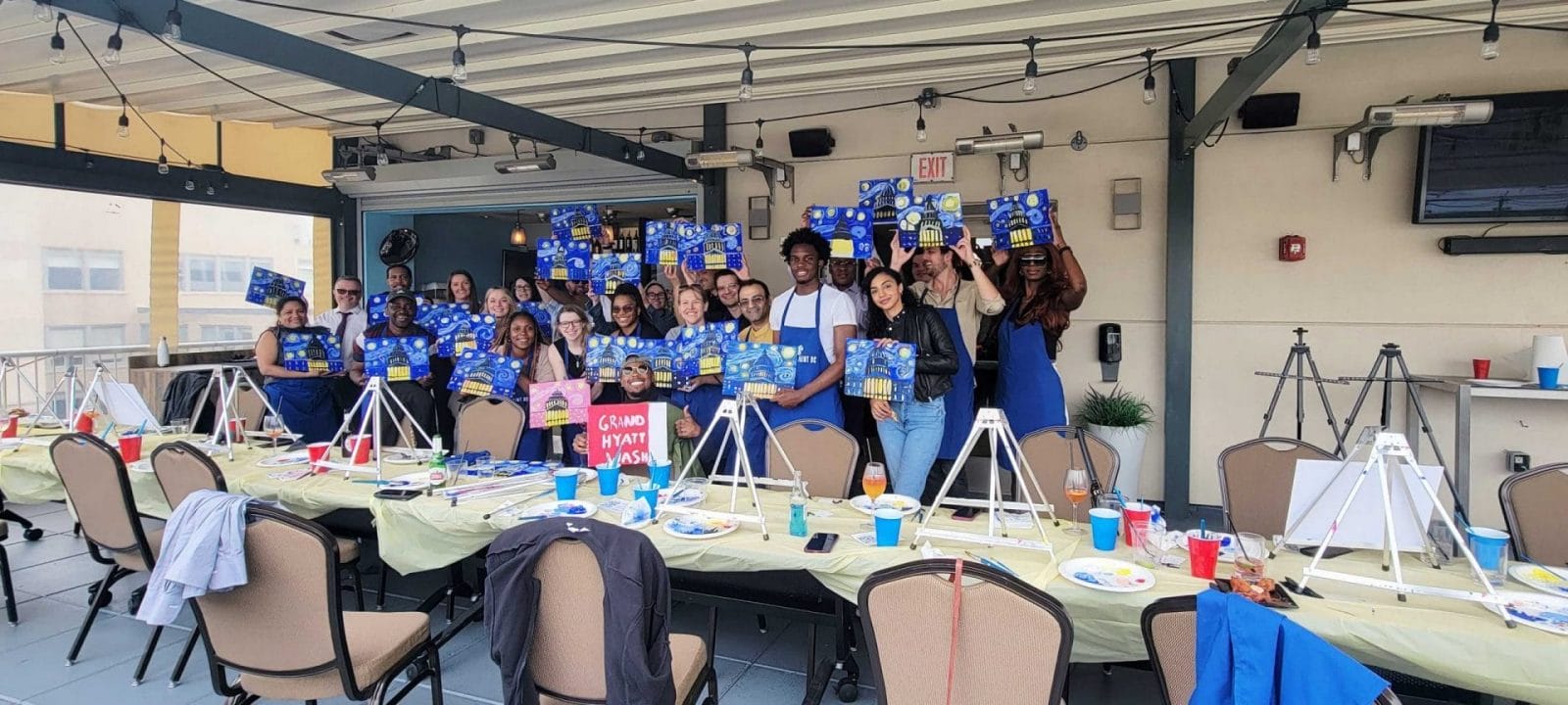 A group of people participating in a paint and sip night, showcasing their creations at a restaurant