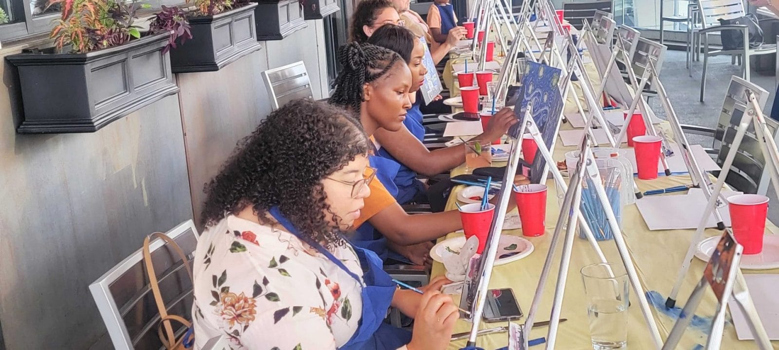 A group of people engaging in a paint and sip activity at a table.