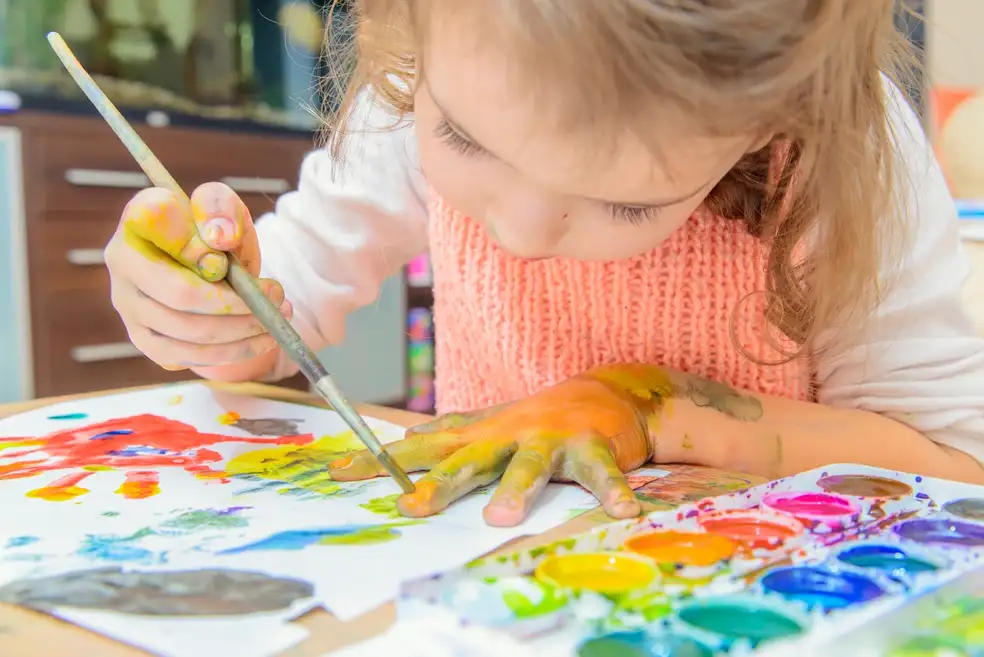 A little girl in DC is sip and paint on a table.