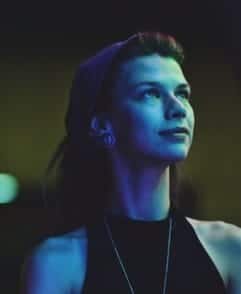 A woman gazes upwards with a pensive look, bathed in striking purple and green light: A Sip and Paint event in DC.