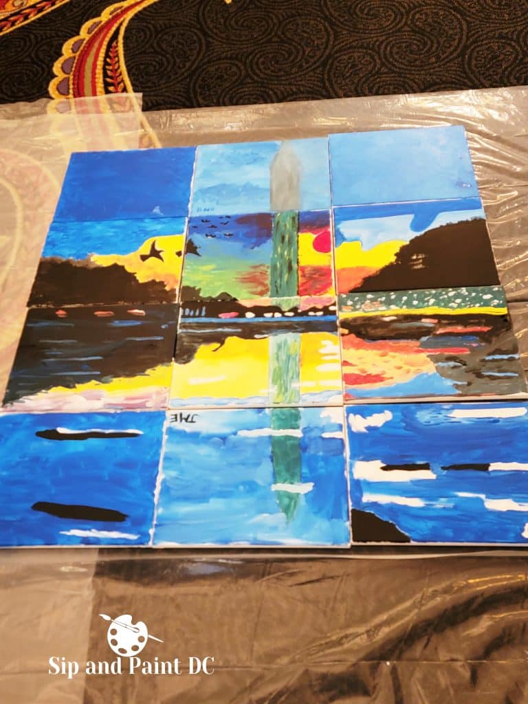 A collection of painted canvases arranged to form an abstract depiction of a monument against a colorful sky and water reflection, created at a Sip and Paint DC event.