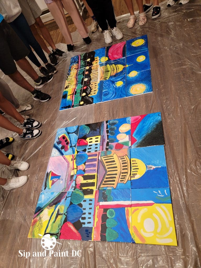 Participants at a sip and paint event stand around two large collaborative paintings featuring vibrant depictions of the US Capitol and night skies.